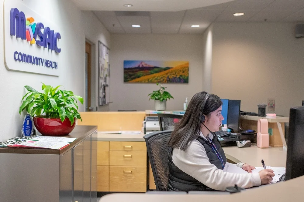 Mosaic Empleado de recepción de «Community Health» con unos auriculares y trabajando delante de un ordenador