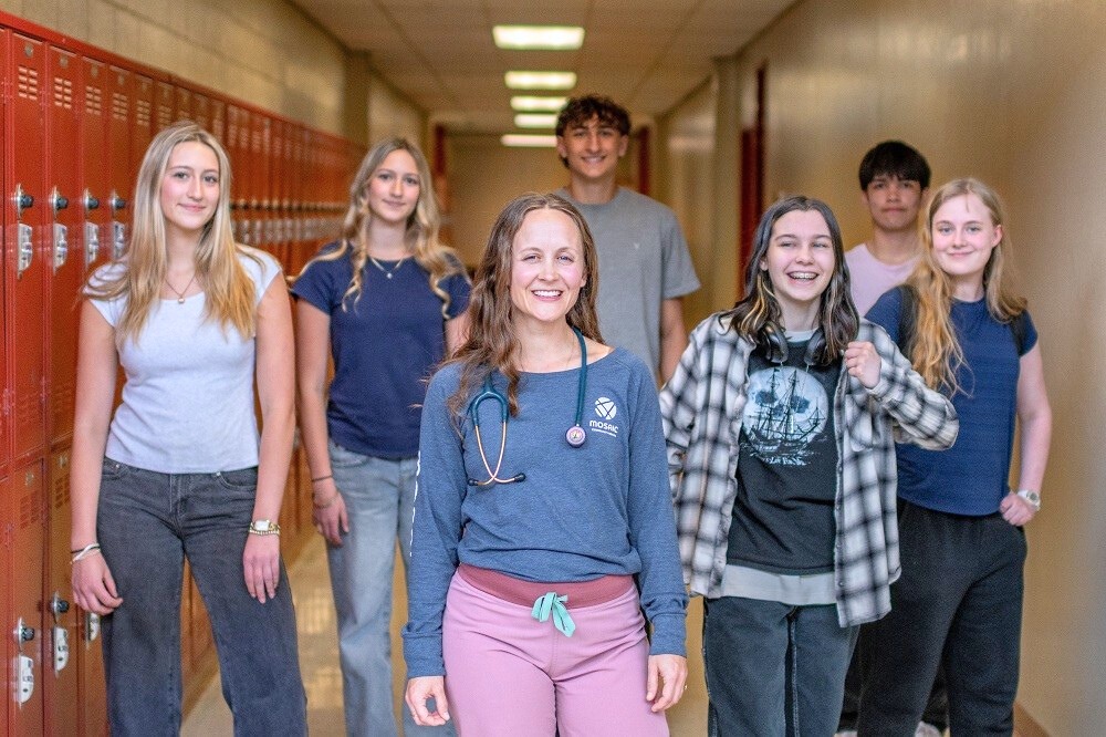 A provider walks with a group of teenage students through the hallway of Bend High School.