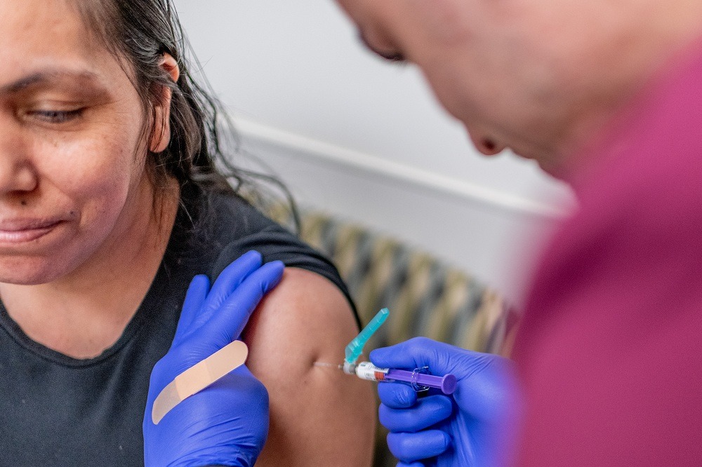 Close-up of a woman receiving a vaccination in her upper arm while a healthcare worker wearing blue gloves administers the injection.