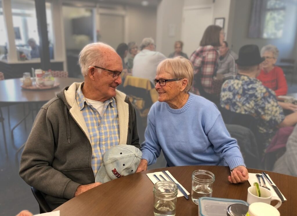 Older couple looking at one another affectionately during a community lunch.