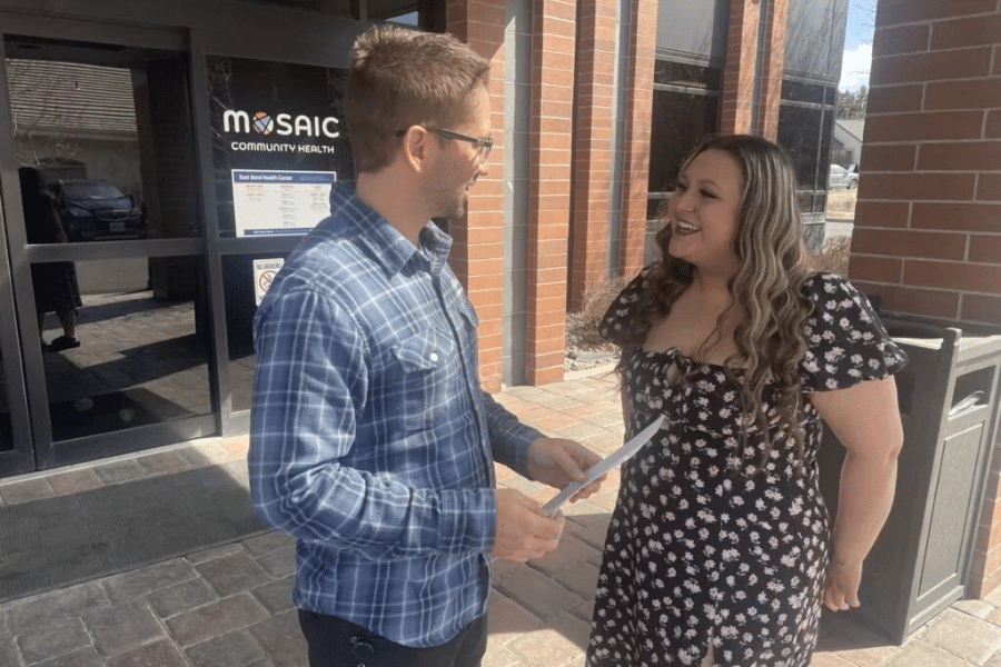 Mosaic Community Health worker Kyle stands with patient Natali outside the doors of the health center.