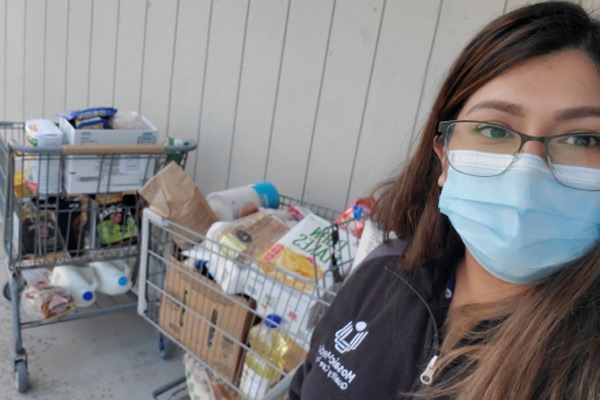 Person wearing mask standing next to groceries for patients