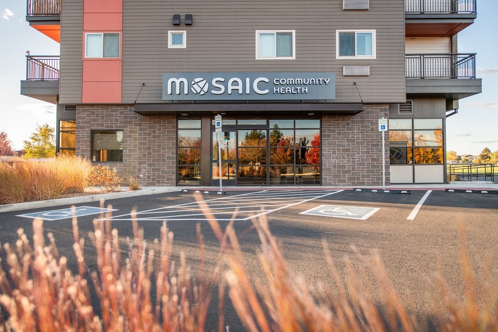 Exterior del centro de salud Mosaic Health en Redmond, con el letrero del edificio sobre la entrada y plazas de aparcamiento accesibles delante de la clínica.