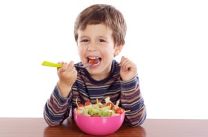 Young boy smiling while eating vegetables